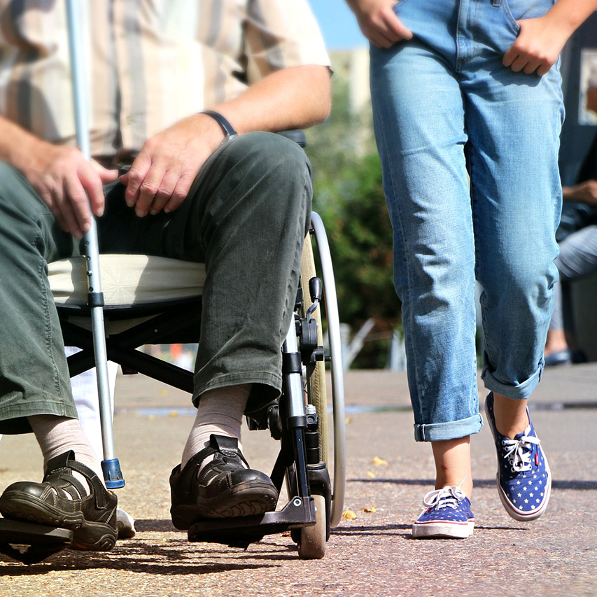 Older man in a wheelchair walking with child.